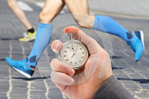 Measuring the running speed of an athlete using a mechanical stopwatch. hand with a stopwatch on the background of the legs of a