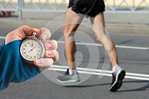 Measuring the running speed of an athlete using a mechanical stopwatch. hand with a stopwatch on the background of the legs of a