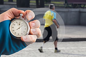 Measuring the running speed of an athlete using a mechanical stopwatch. hand with a stopwatch on the background of the legs of a