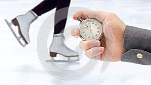 Measuring speed on skates with a stopwatch. hand with a stopwatch on the background of the legs of a man skating on an ice rink