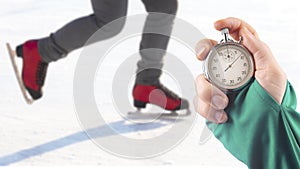 Measuring speed on skates with a stopwatch. hand with a stopwatch on the background of the legs of a man skating on an ice rink