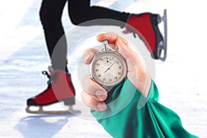 Measuring speed on skates with a stopwatch. hand with a stopwatch on the background of the legs of a man skating on an ice rink
