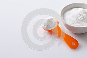 Measuring spoon with artificial sweetener aspartame E951 and a bowl of blemish on a white glossy background