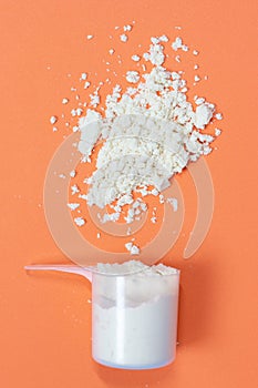 Measuring spoon with scattered protein powder on a orange background