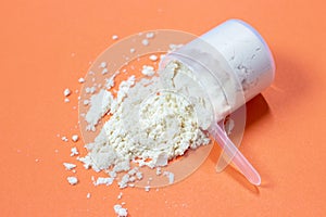 Measuring spoon with scattered protein powder, side view on a orange background
