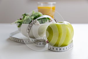 Measuring tape around the apple, bowl of green salad and glass of juice. Weight loss and right nutrition concept