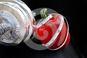 Measuring tape curl up on a Red Sweet Pepper with Silver Dumbbell