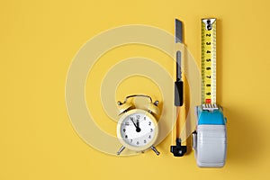 Measuring tape, cutter knife and clock  over yellow bakground. Carpenter and Construct concept.