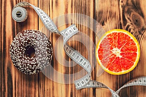 Measuring tape dividing wooden surface between chocolate donut and orange, choice between healthy and unhealthy food