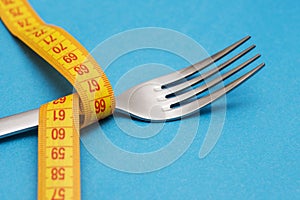 Measuring tape with fork on blue background. Concept of weight loss. Weight management. Healthy lifestyle. Weight loss health