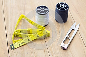 Measuring tape scissor and thread on wooden board