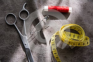 Measuring tape, scissors and reel of red thread on gray fabric