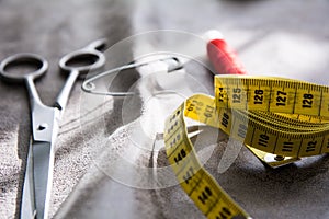 Measuring tape, scissors and reel of red thread on gray fabric