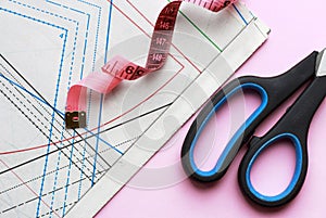 Measuring tape, scissors and sewing pattern for sewing on a pink background close-up, top view