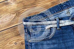 Measuring tape for weight loss in jeans on a wooden background. The concept of being overweight. Selective focus