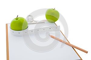 Measuring tape wrapped around a green apple and clipboard