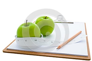 Measuring tape wrapped around a green apple and clipboard