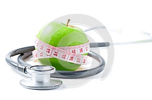 Measuring tape wrapped around a green apple with  stethoscope isolated on white