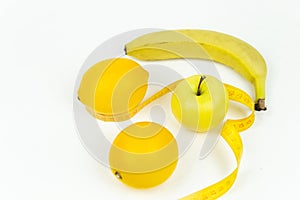 A measuring tape wrapped around a green apple and two lemons and a banana as a symbol of diet.
