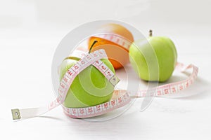 Measuring tape wrapped around two green apple and orange isolated on white background, Concept of the goal to lose