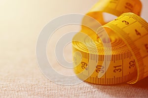 The measuring tape of yellow color with numerical indicators in the form of centimeters or inches lies on a gray knitted fabric.