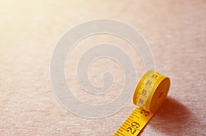 The measuring tape of yellow color with numerical indicators in the form of centimeters or inches lies on a gray knitted fabric.