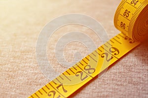 The measuring tape of yellow color with numerical indicators in the form of centimeters or inches lies on a gray knitted fabric.