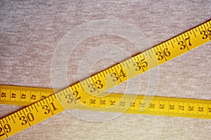 The measuring tape of yellow color with numerical indicators in the form of centimeters or inches lies on a gray knitted fabric.