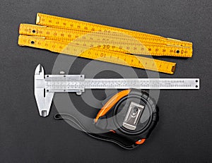 Measuring tools on black: ruler, caliper and tape