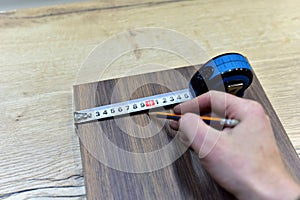 Measuring the width wooden Panel using a construction tape. Dimensioning with a pencil on the medium density fiberboard (MDF).