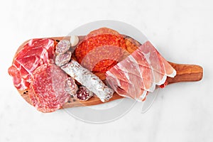 Meat appetizer platter, above view on a serving board against white marble