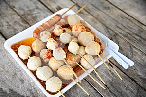 Meat ball , fish ball and sausage hotdog grilled on stick on tray with wooden background Thai style food