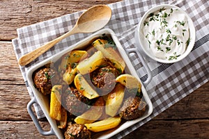 Meat balls with potato wedges in a baking dish and sour cream cl