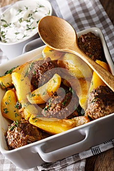 Meat balls with potatoes in a baking dish and sour cream close-up on a table. Vertical