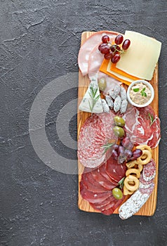 Meat board with products from the Italian region to wine - sausages, cheeses, bread, fresh vegetables, green herbs, and grapes - photo