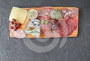 Meat board with products from the Italian region to wine - sausages, cheeses, bread, fresh vegetables, green herbs, and grapes - photo