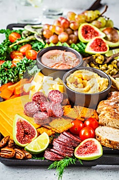 Meat and cheese appetizer platter. Sausage, cheese, hummus, vegetables, fruits and bread on black tray