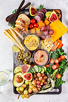 Meat and cheese appetizer platter. Sausage, cheese, hummus, vegetables, fruits and bread on black tray