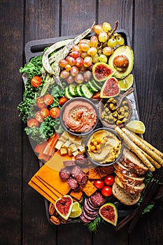 Meat and cheese appetizer platter. Sausage, cheese, hummus, vegetables, fruits and bread on black tray