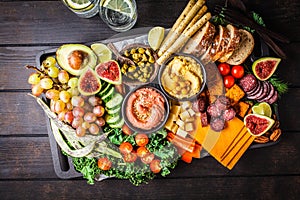 Meat and cheese appetizer platter. Sausage, cheese, hummus, vegetables, fruits and bread on black tray