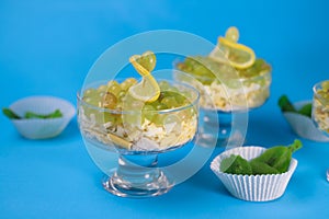meat chicken salad in layers in a transparent glass with green grapes and lemon slices next to kiwi on a blue background