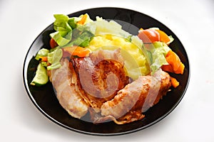 Meat dish bacon with potato side dish and salad with tomatoes, lettuce and cucumber on a black plate