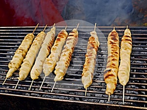 Meat dish wrapped in dough around wooden sticks is grilled