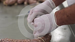 Meat factory work. Male worker ties meat with net. Sausage making process.