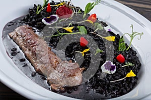 Meat with a garnish in white plate. lamb with pearl barley with cuttlefish ink. Eastern cuisine