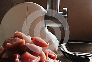 Meat grinder and raw meat pieces in kitchen