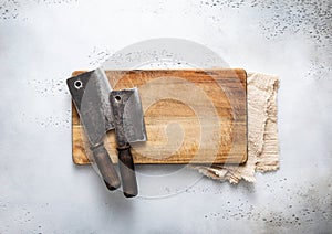Meat hatchets on scratched cutting board and kitchen towel on light background. Top view