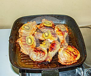 Meat with kiwi fruit. Fried chicken pieces with kiwi slices on a grill pan