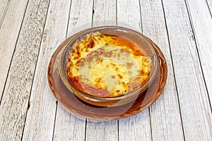 Meat lasagna with bÃ©chamel gratin in clay pot and clay plate on light wooden table