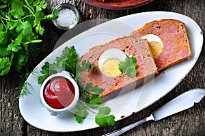 Meat loaf with boiled egg, tomato sauce, coriander and parsley on a wooden table. rustic style.